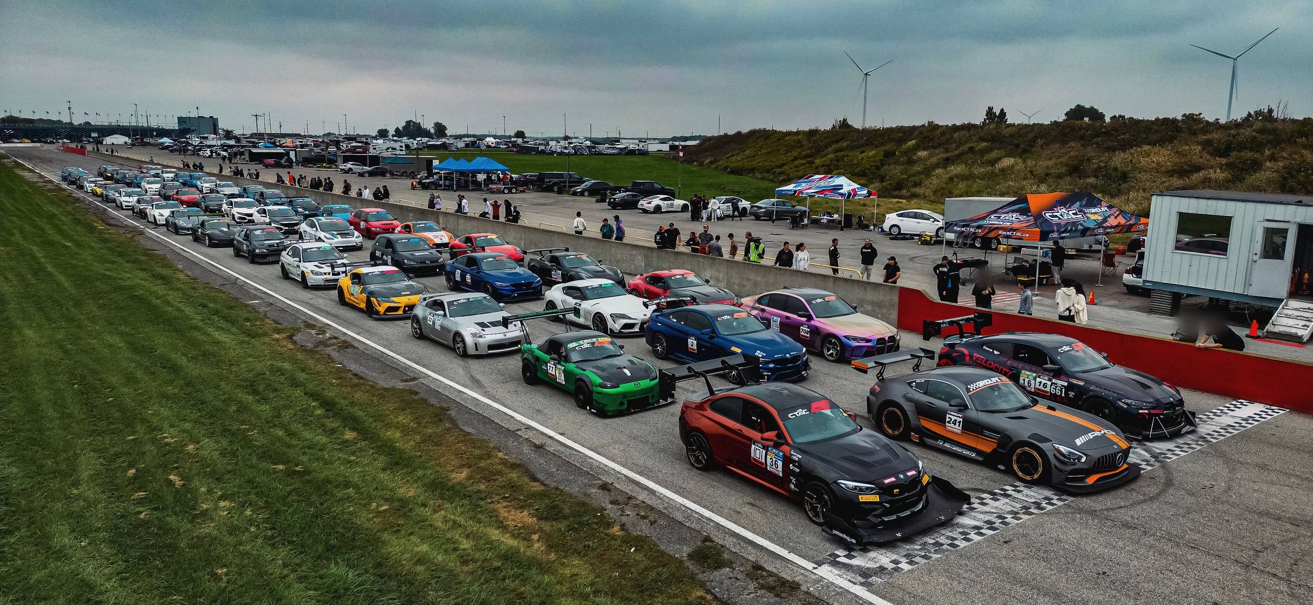 Aerial view of a Canadian Time Attack Challenge event at Toronto Motorsports Park, Cayuga, Ontario, in September 2023: some 60 cars lined up on the front straight beside the paddock, where a YD Auto Group tent stands among the team tents.