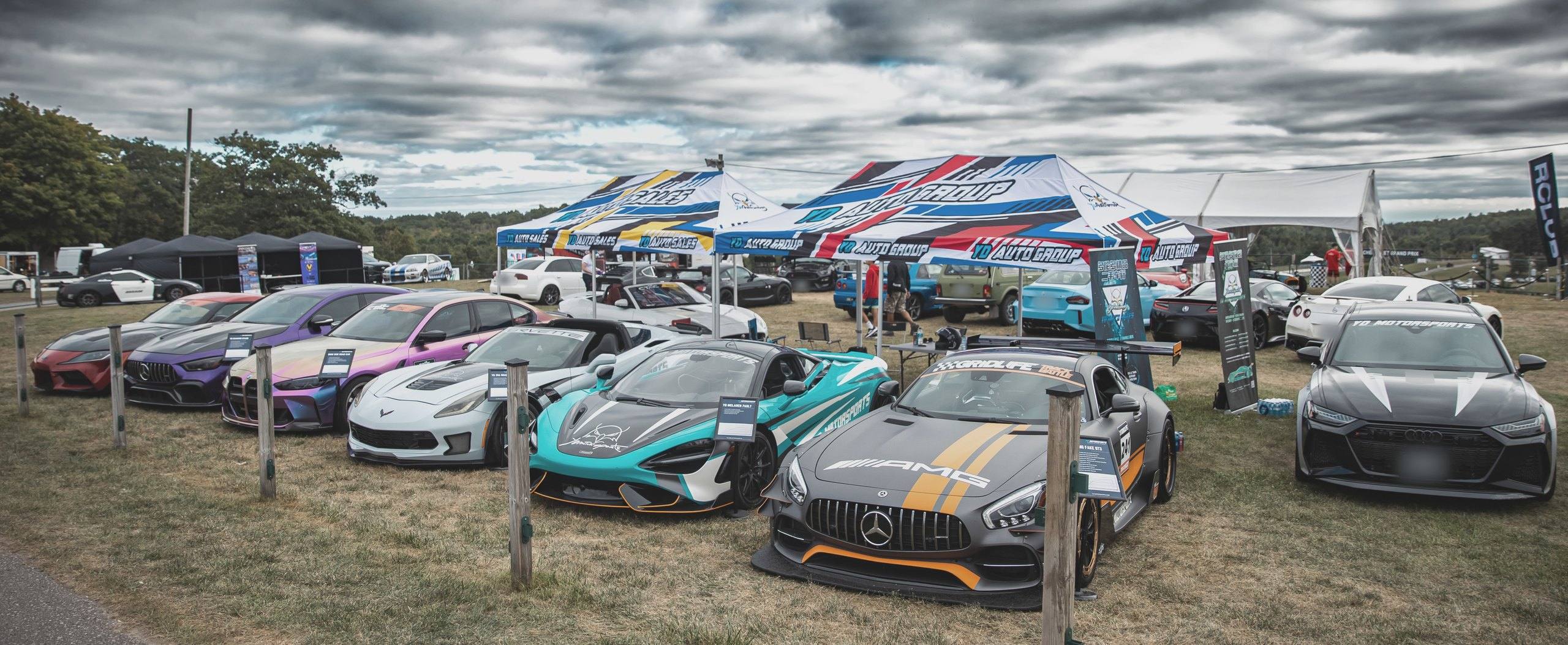 YD display at the Drive Festival, Canadian Tire Motorsport Park, Bowmanville, Ontario, in September 2023: a row of vehicles including a McLaren 765LT, a Mercedes-AMG GT4 race car and an Audi RS 7, each with an information placard, under YD Auto Group and YD Auto Sales tents.