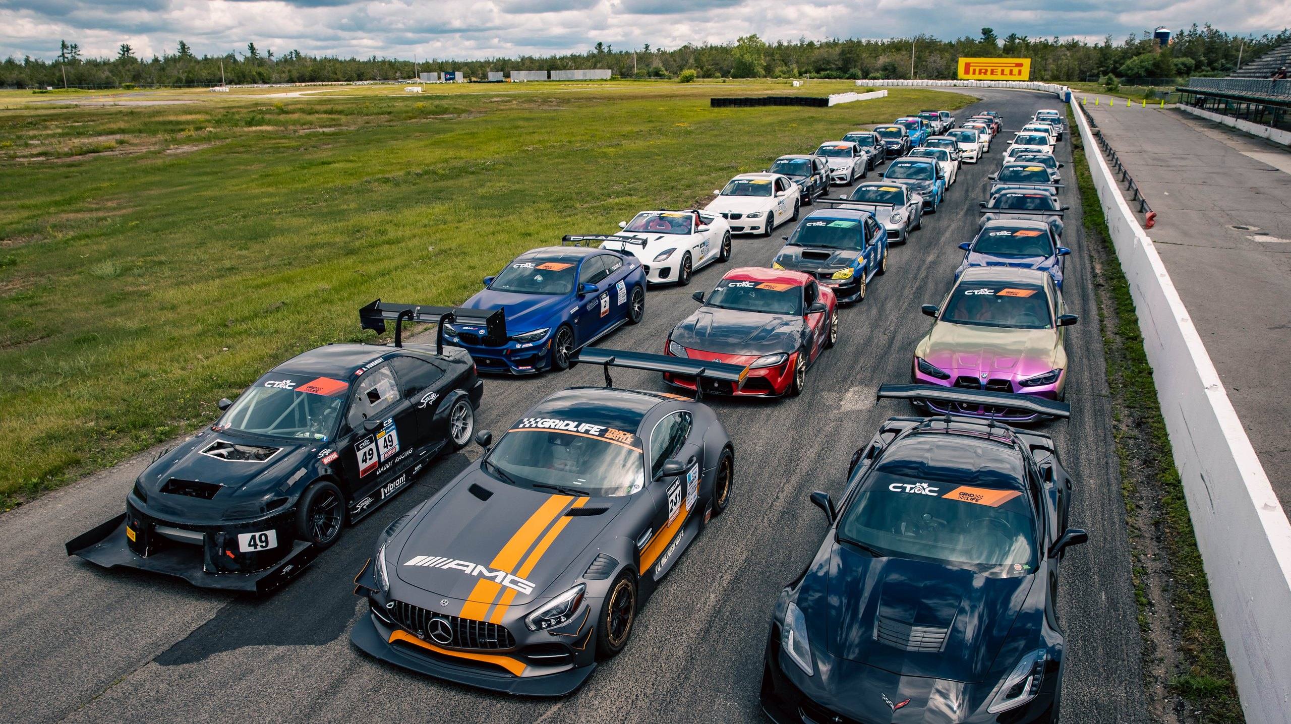 About 30 cars lined up in three columns on the front straight at a Canadian Time Attack Challenge event at Shannonville Motorsport Park, Ontario, in June 2023, led by a Mitsubishi Lancer Evolution, a Mercedes-AMG GT4 and a Chevrolet Corvette.
