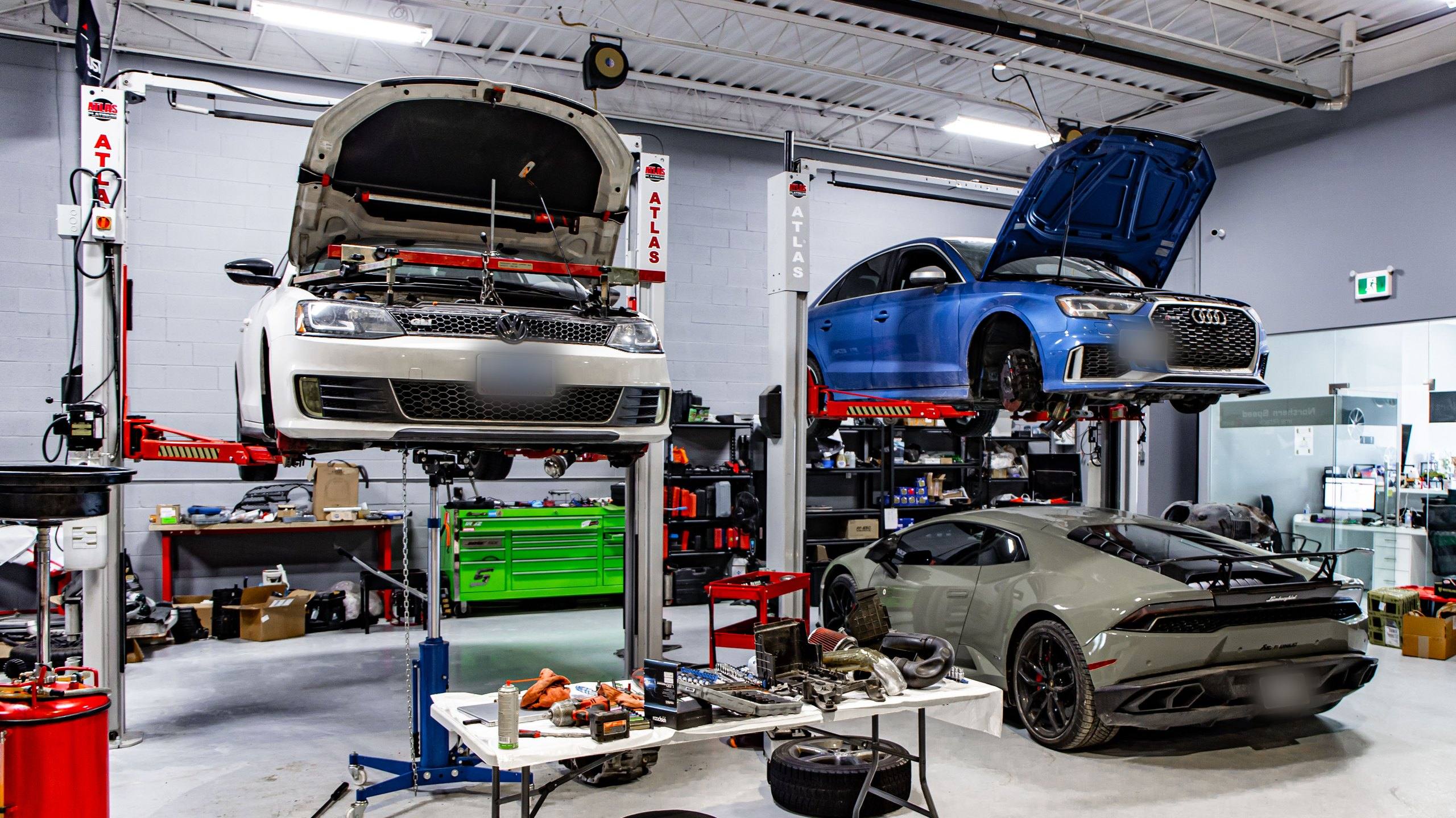Inside the YD Motorsports workshop in Vaughan in February 2021: a Volkswagen Jetta GLI and an Audi RS 3 raised on two-post lifts, a Lamborghini Huracán on the shop floor, and tools and parts laid out on a work table.