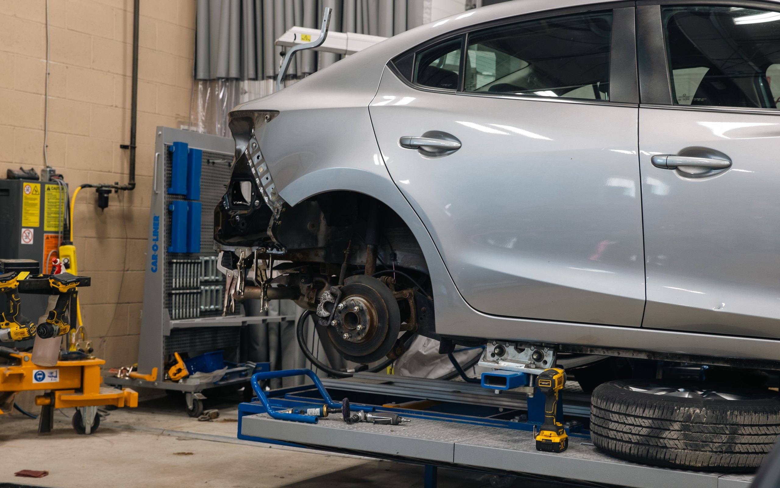 Collision repair bay: a silver sedan secured on a Car-O-Liner frame bench with its rear quarter section cut away for structural repair.