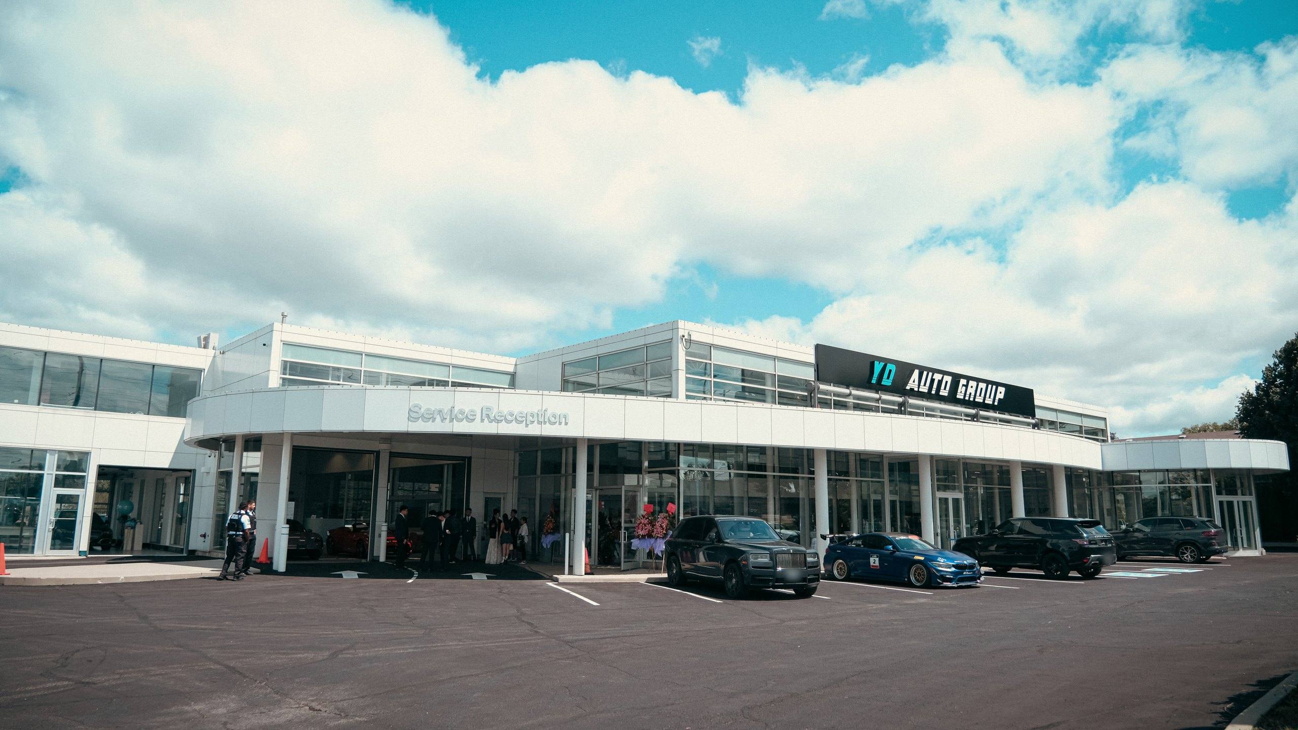 The full frontage of the YD Auto Group headquarters on Mulock Drive, Newmarket, showing the curved Service Reception canopy, the YD Auto Group sign and the showroom glazing on the opening day in July 2024.