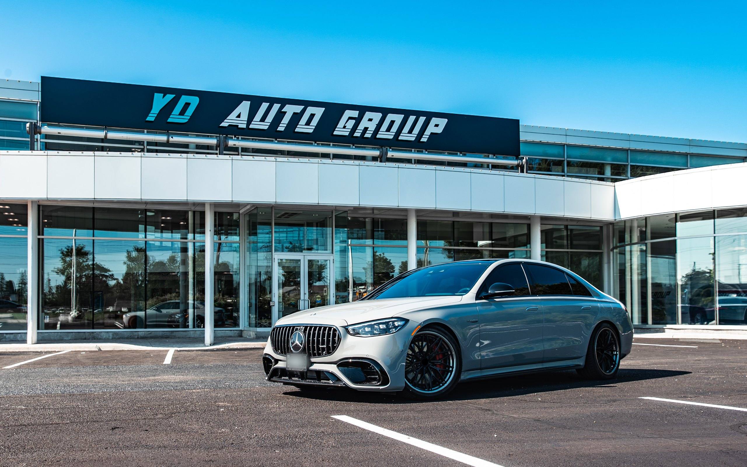 Front elevation of the YD Auto Group headquarters at 87 Mulock Drive, Newmarket, with the YD Auto Group fascia sign above the glazed showroom and a grey Mercedes-AMG S-Class sedan in the forecourt.