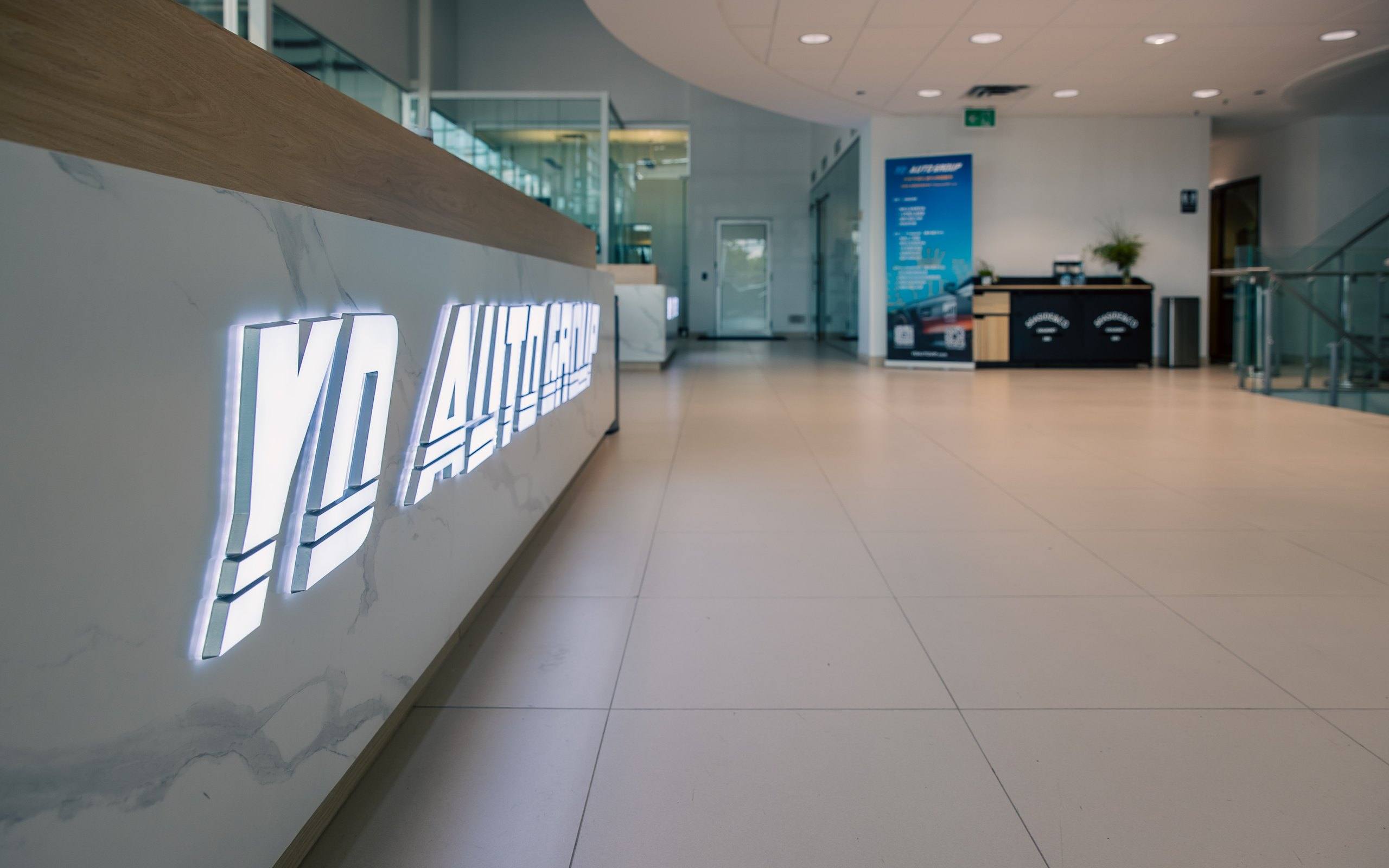 Backlit YD Auto Group lettering on the marble-clad reception counter in the headquarters lobby.