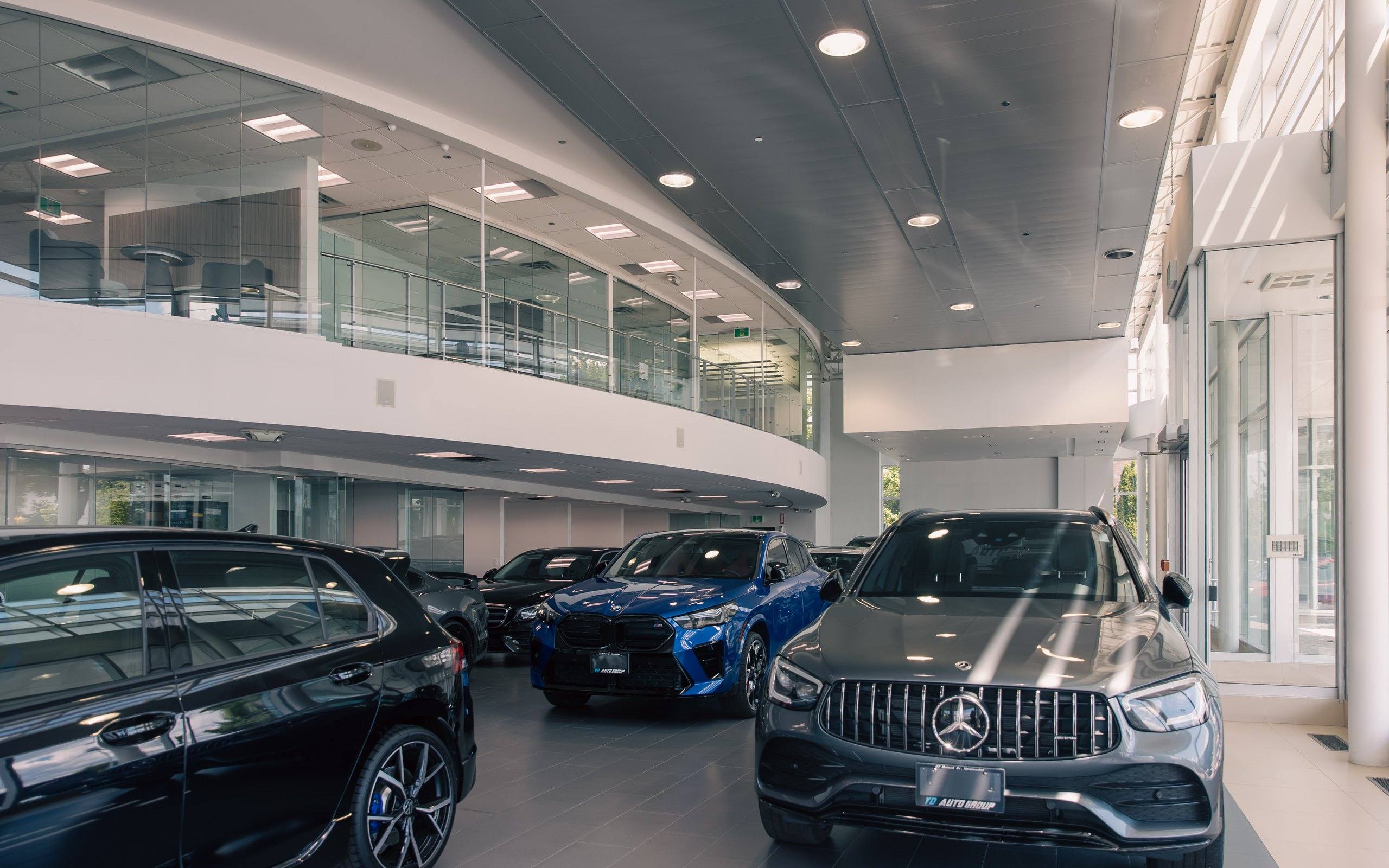 Showroom floor with a Mercedes-AMG GLC, a blue BMW M sport utility vehicle and other vehicles on display beneath the curved glass mezzanine.