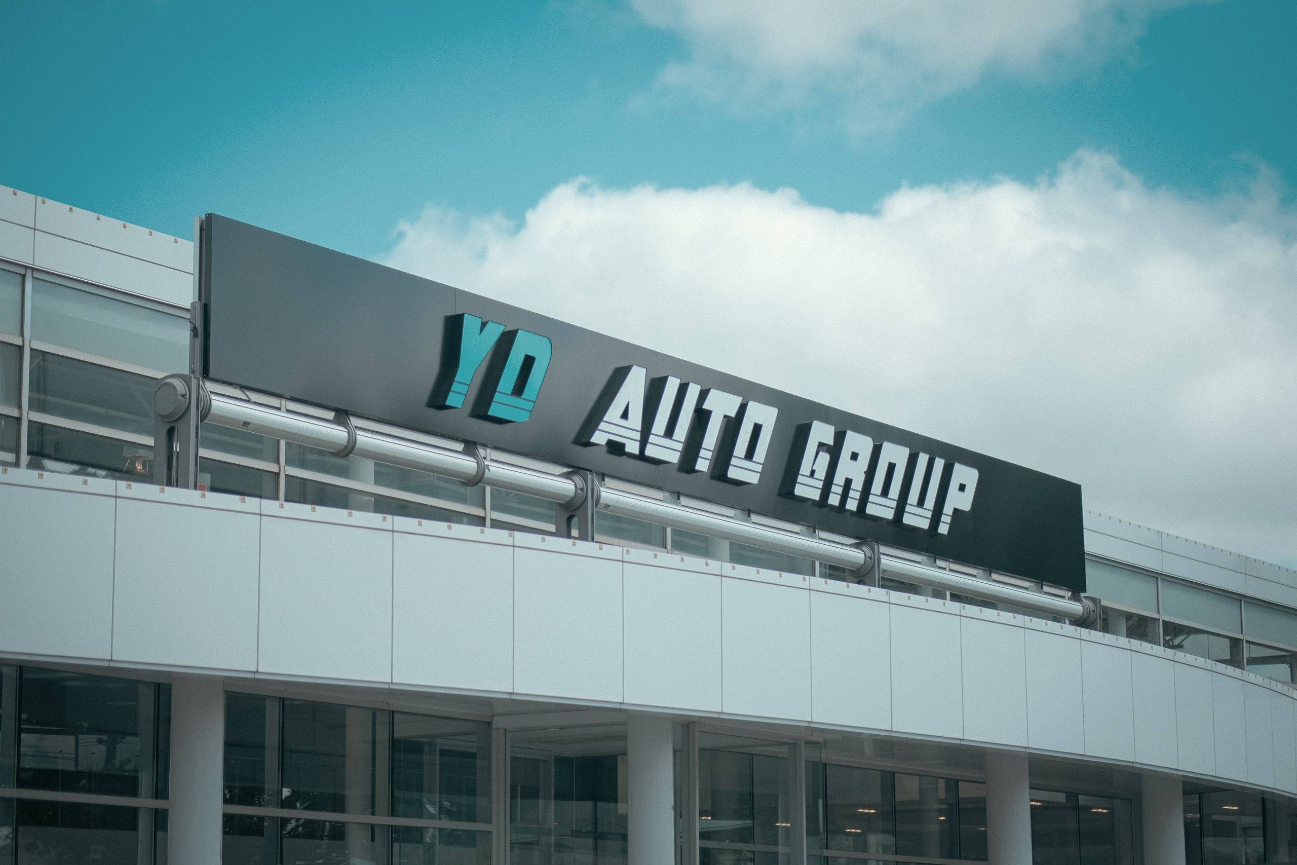 Dimensional YD Auto Group lettering on the fascia sign above the curved white façade of the Newmarket headquarters.