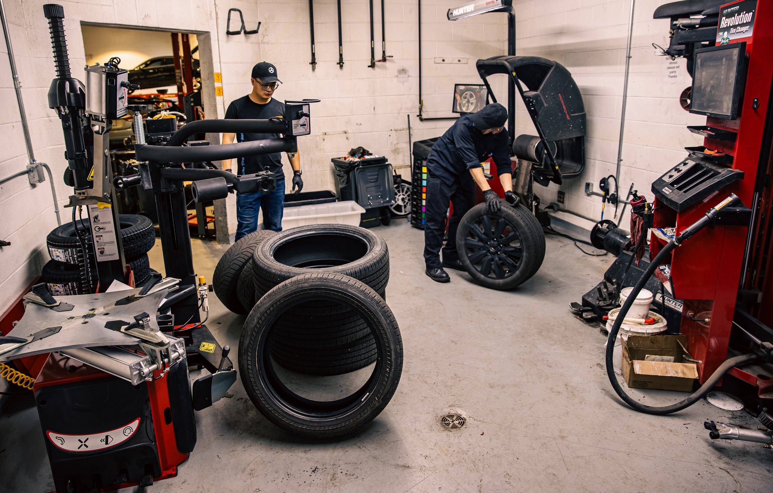Tire service room equipped with Hunter tire changers and a wheel balancer, where two technicians handle a set of tires and a wheel.