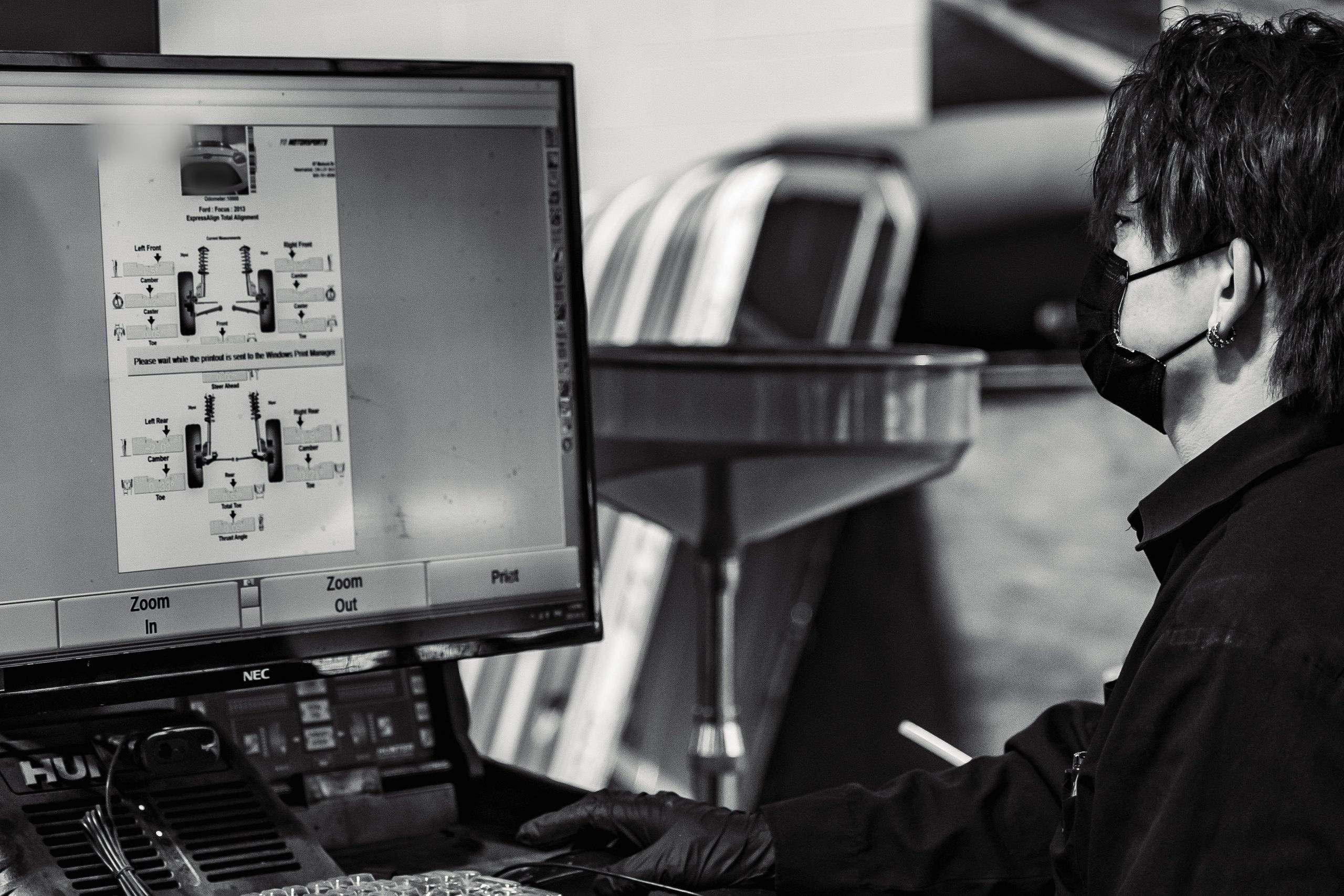 Technician reviewing a four-wheel alignment report on a Hunter alignment console, black-and-white photograph.