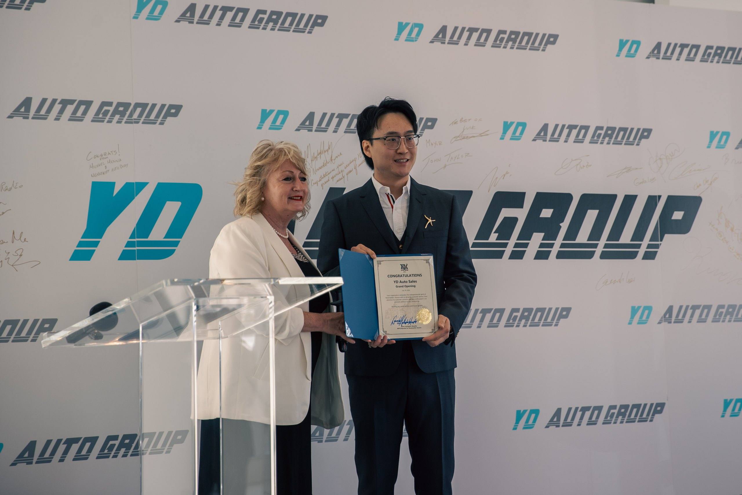 Certificate of congratulations on the grand opening of YD Auto Sales from Dawn Gallagher Murphy, MPP for Newmarket–Aurora, presented on stage on July 18, 2024.