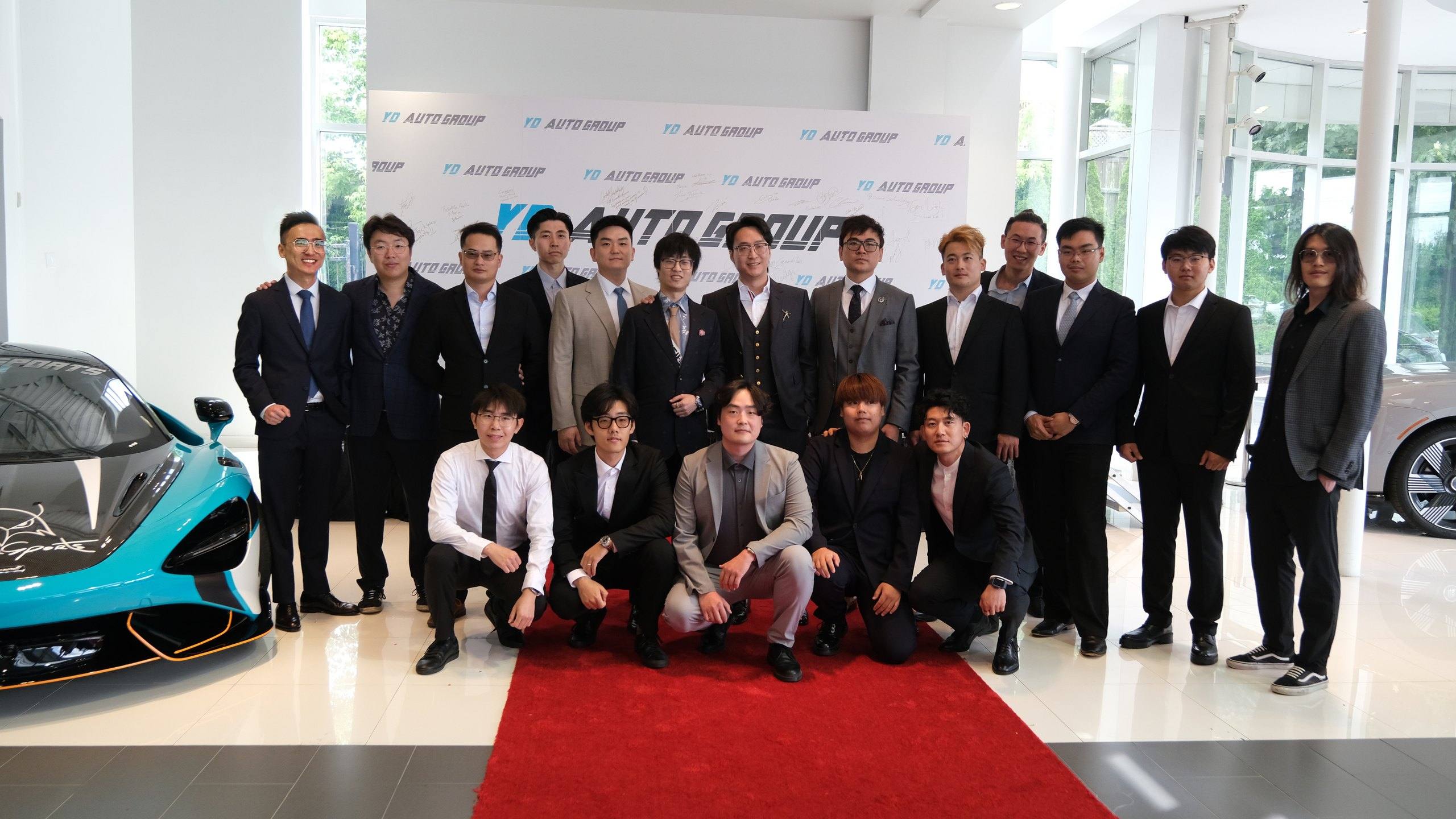 YD Auto Group staff in business attire gathered in the showroom in front of the signed company backdrop at the July 2024 grand opening.